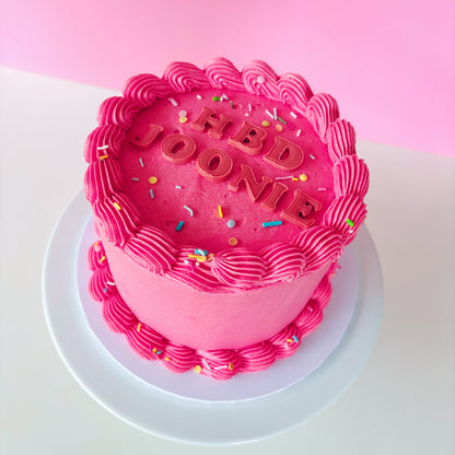 Pink 6 inch cake with 'HBD' fondant letters and sprinkles