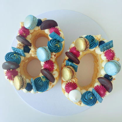 Decorative number '80' vanilla cake with colorful icing and macarons.