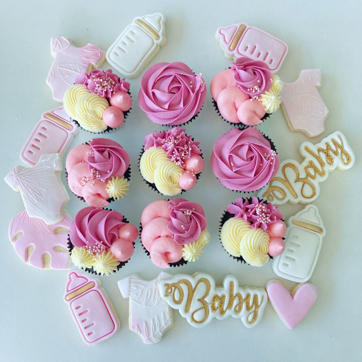 Pink baby shower cupcakes with pink frosting, baby girl embossed cookies, and 'Baby' letter decorations with sprinkles