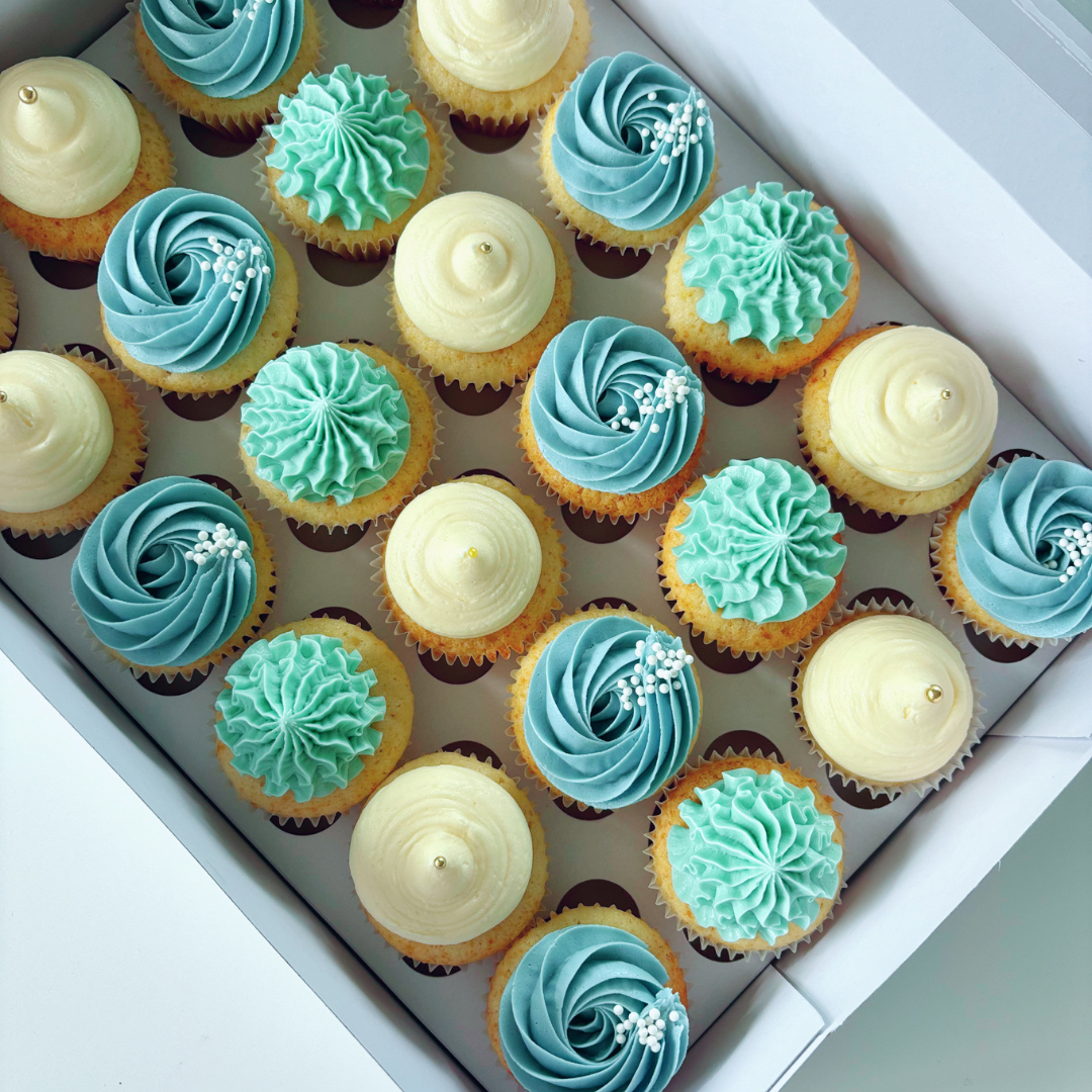 Assorted mini cupcakes with blue, green, and white buttercream frosting in a box.