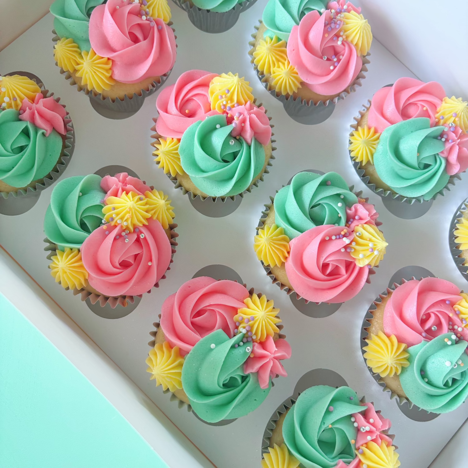 Vanilla cupcakes with Green, pink & yellow buttercream frosting & sprinkles.