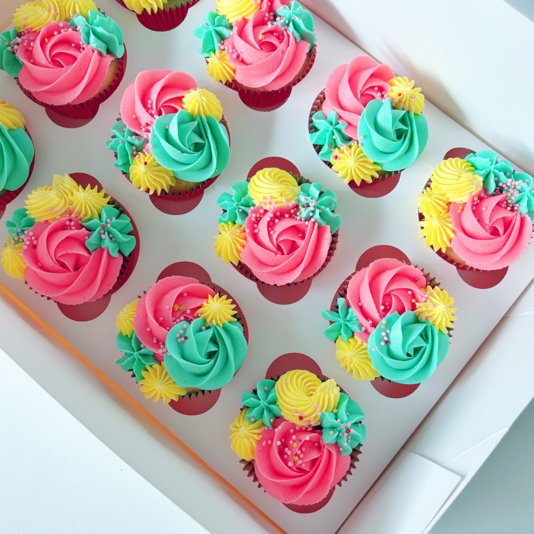 Colourful cupcakes with pink, green, and yellow frosting in a box.