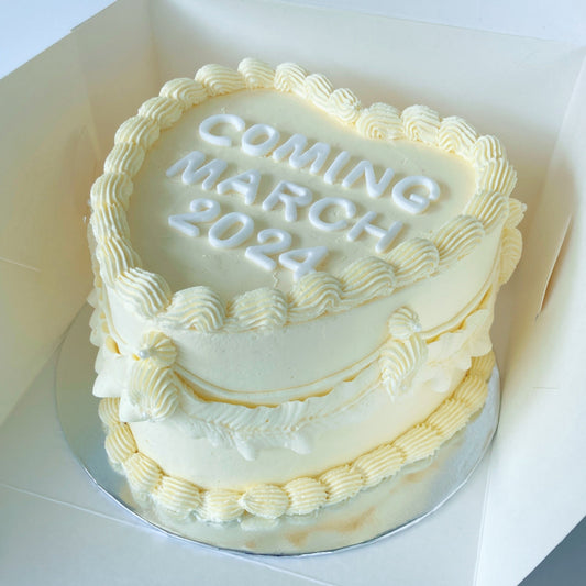 Gender reveal white vintage 8 inch heart cake with white buttercream and fondant letters 'COMING MARCH 2024' text on top