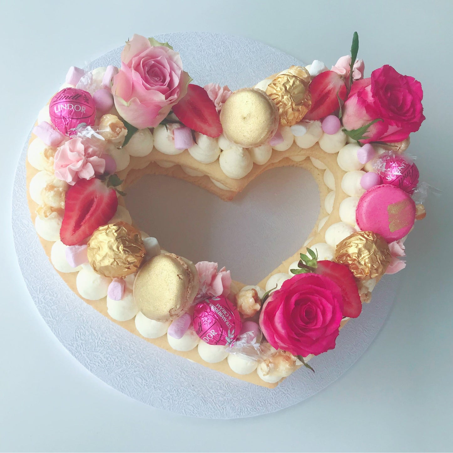 Heart-shaped cake decorated with flowers, chocolates, and pink roses 