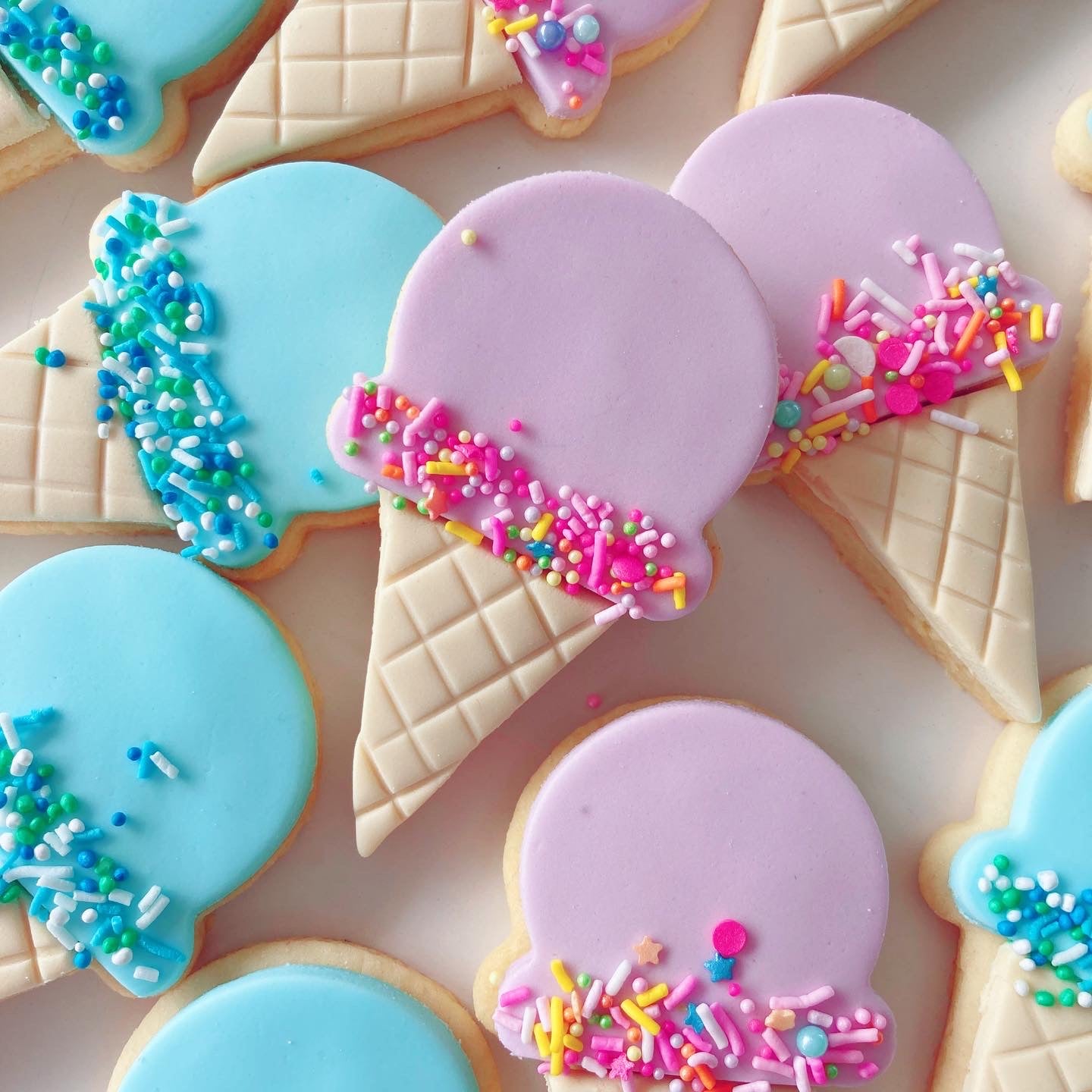 Colorful decorated blue & pink cookies shaped like ice cream cones with sprinkles