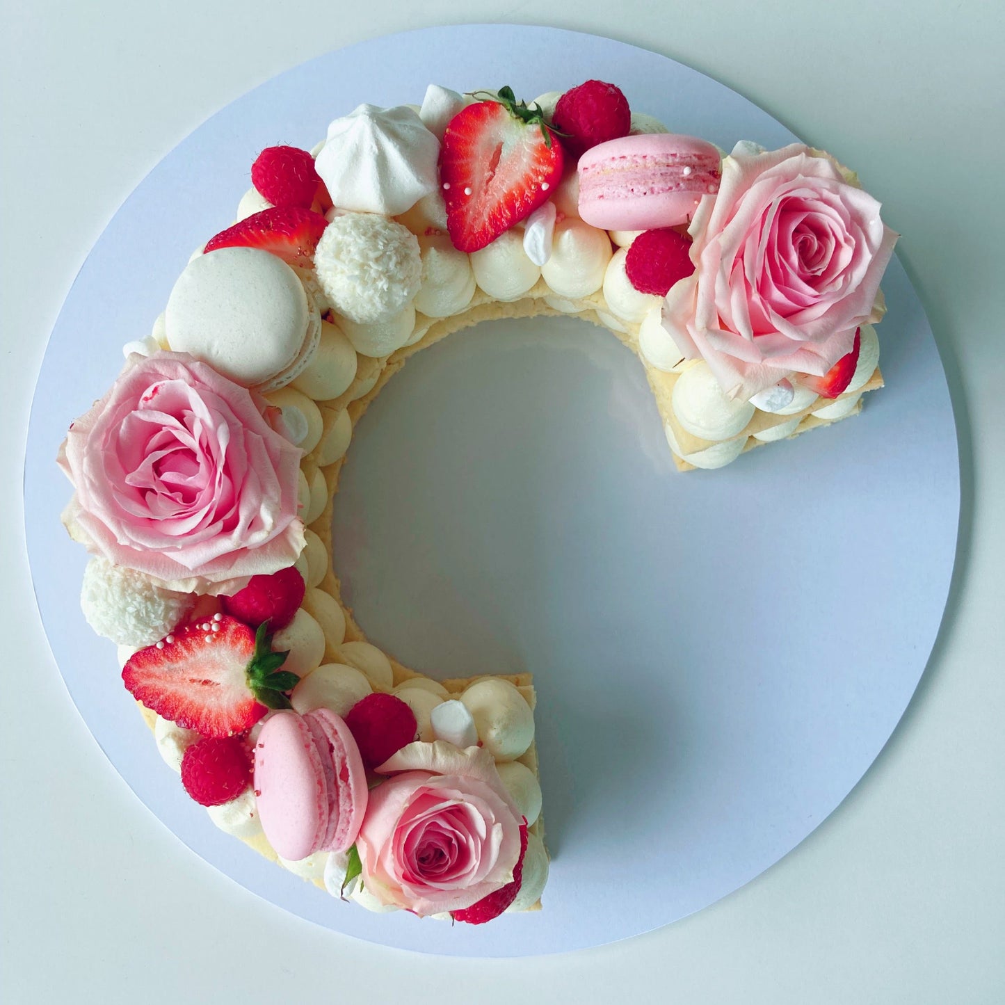Cookie cake shaped like the letter C with pink roses, strawberries, and macarons.