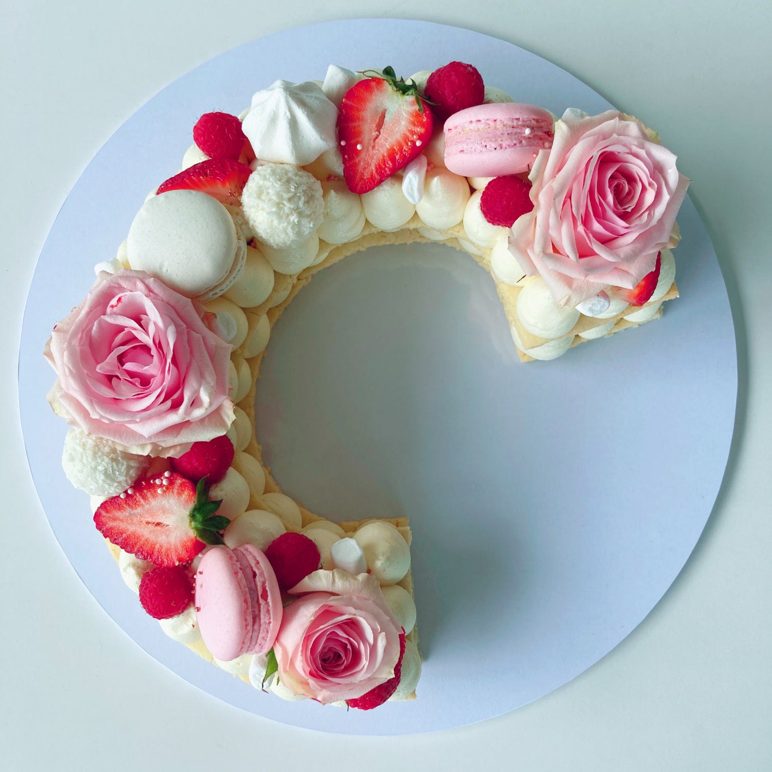 Cookie cake shaped like the letter C with pink roses, strawberries, and macarons.