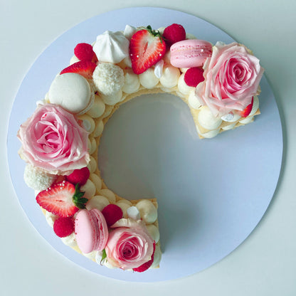 Cookie cake shaped like the letter C with pink roses, strawberries, and macarons.