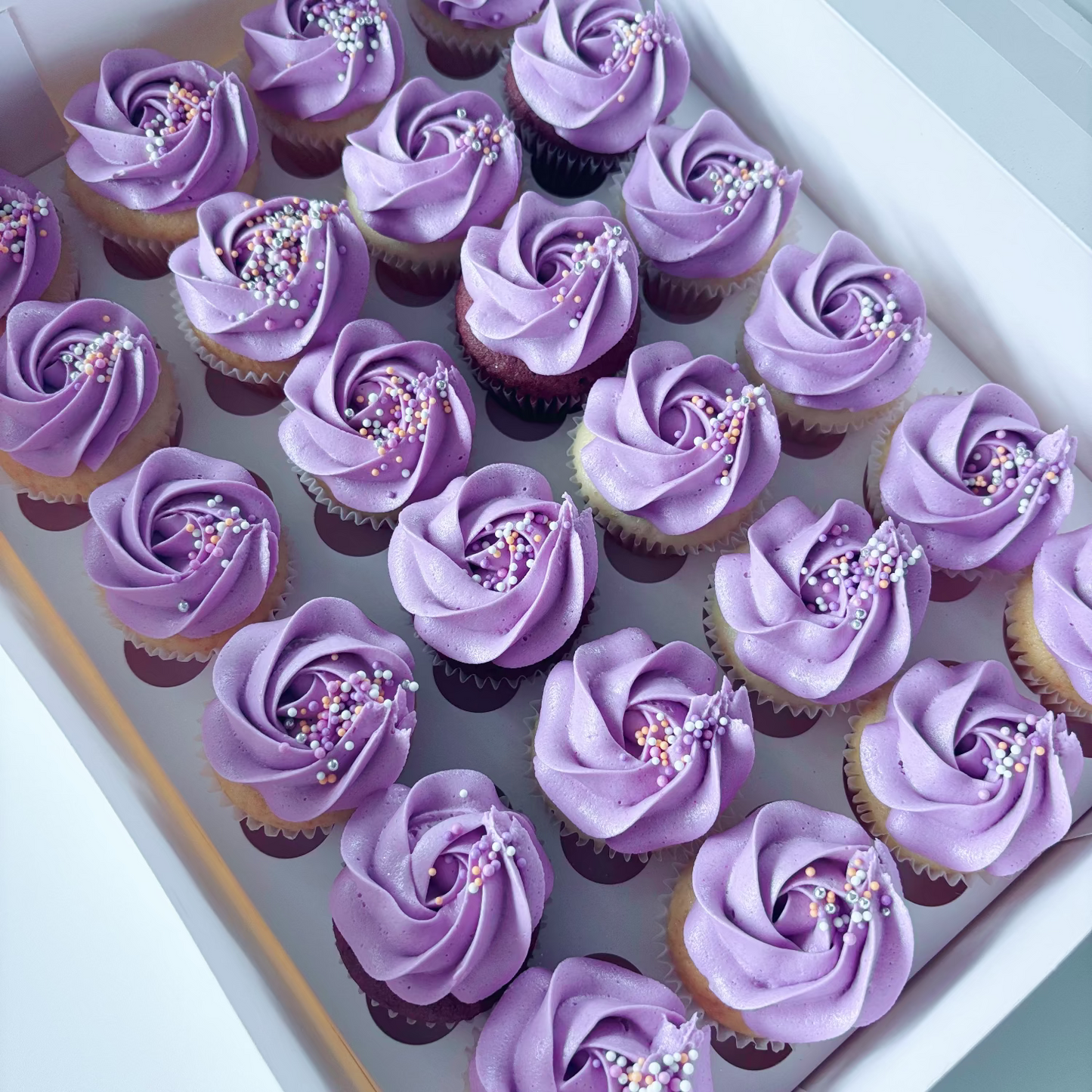 Box of 24 vanila cupcakes with purple frosting and sprinkles