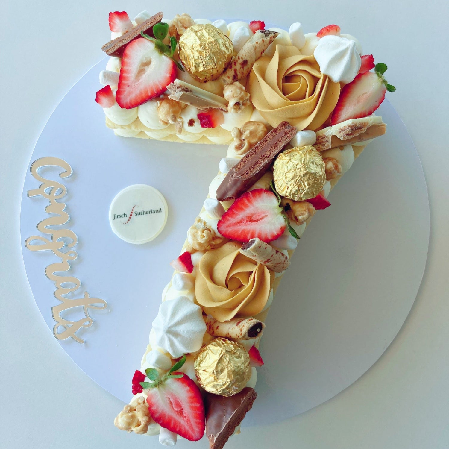 Cookie cake shaped like a number '7' with strawberries, gold leaves, and other toppings.