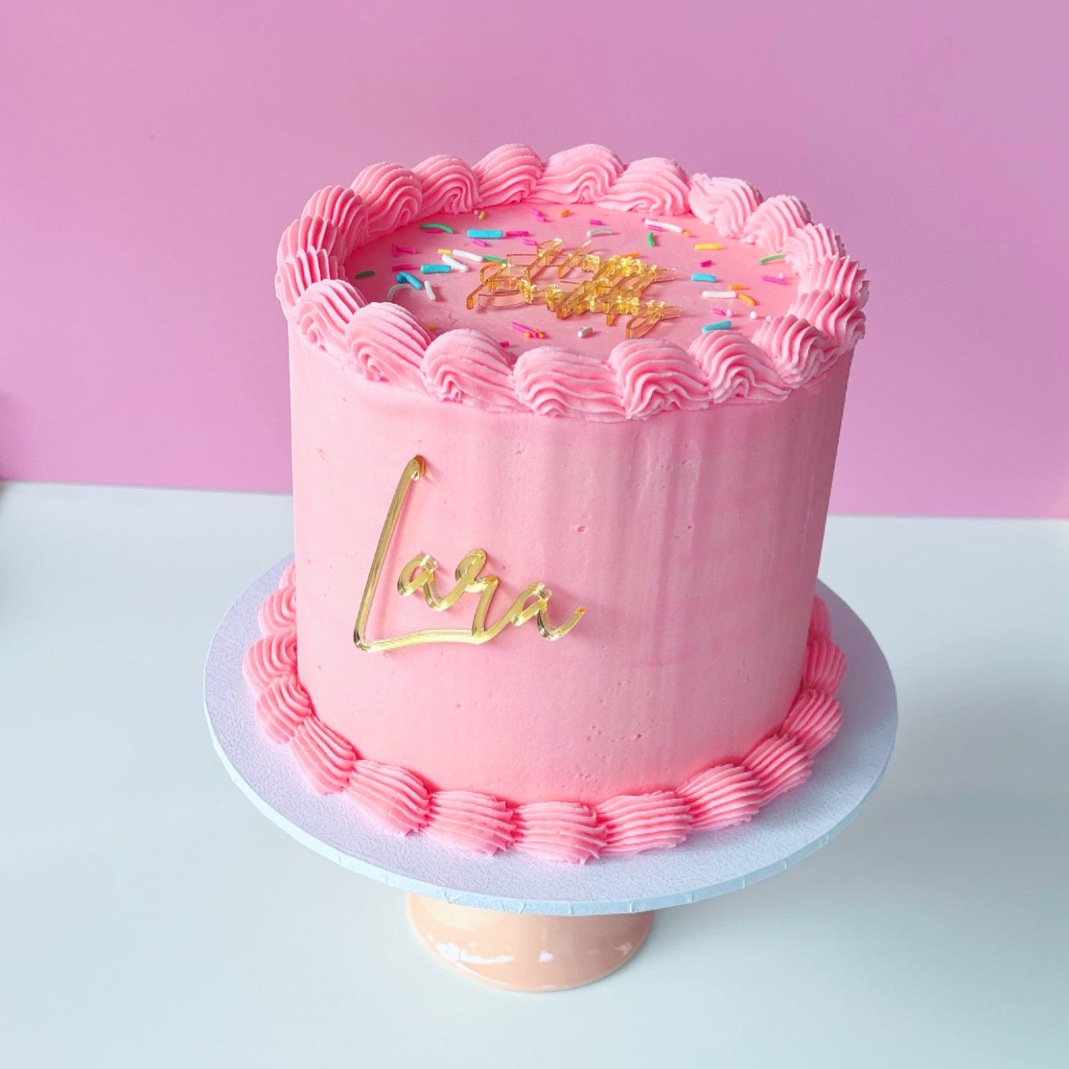4 inch round cake with pink vintage buttercream piping and mirror gold acrylic toppers