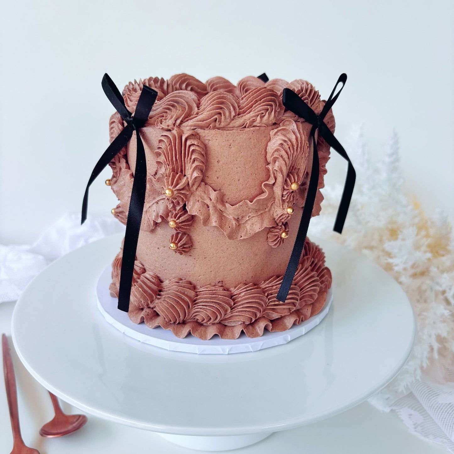 Chocolate vintage 4 inch cake with intricate piping and black bows.