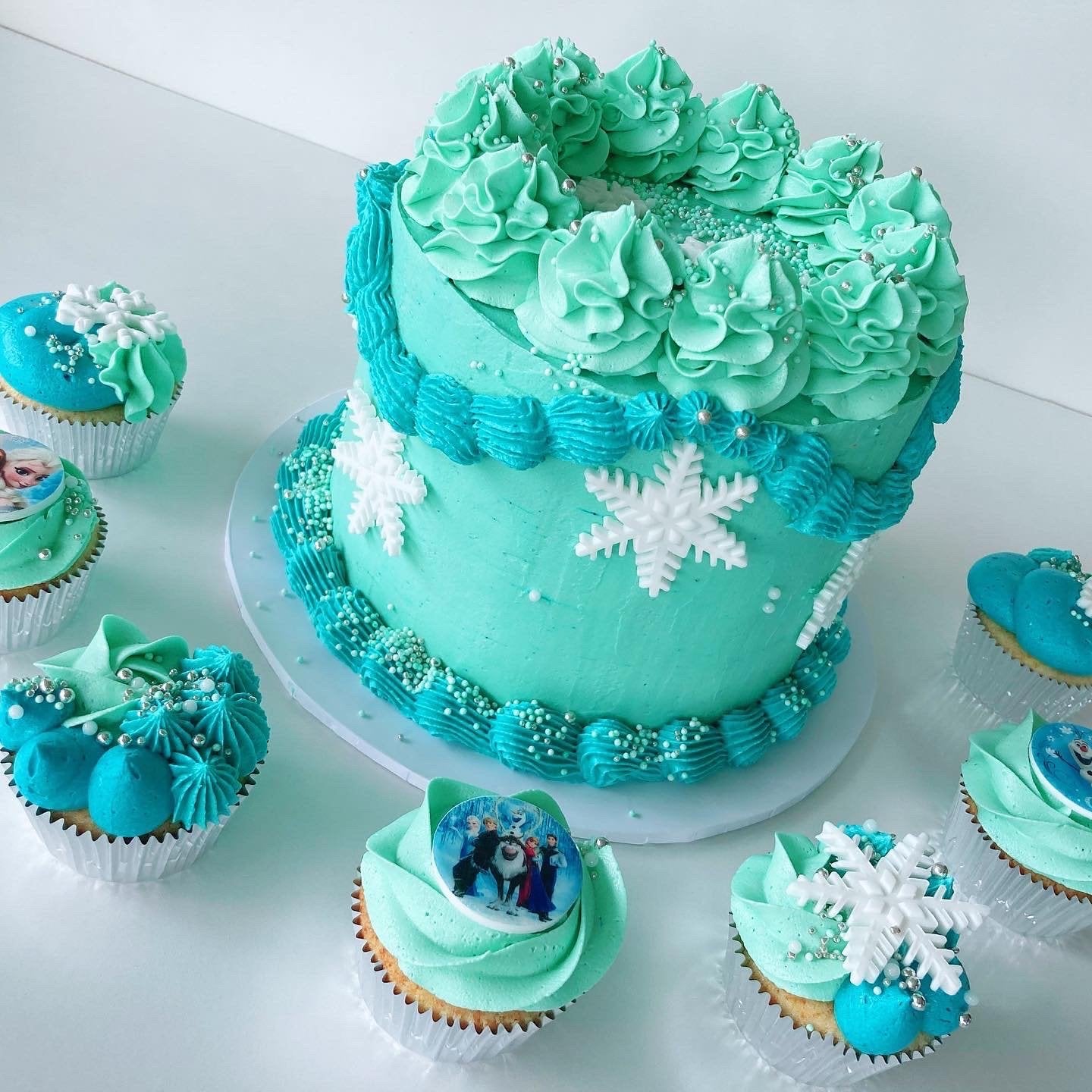 Teal Frozen themed cake with snowflake decorations surrounded by matching cupcakes with edible images.